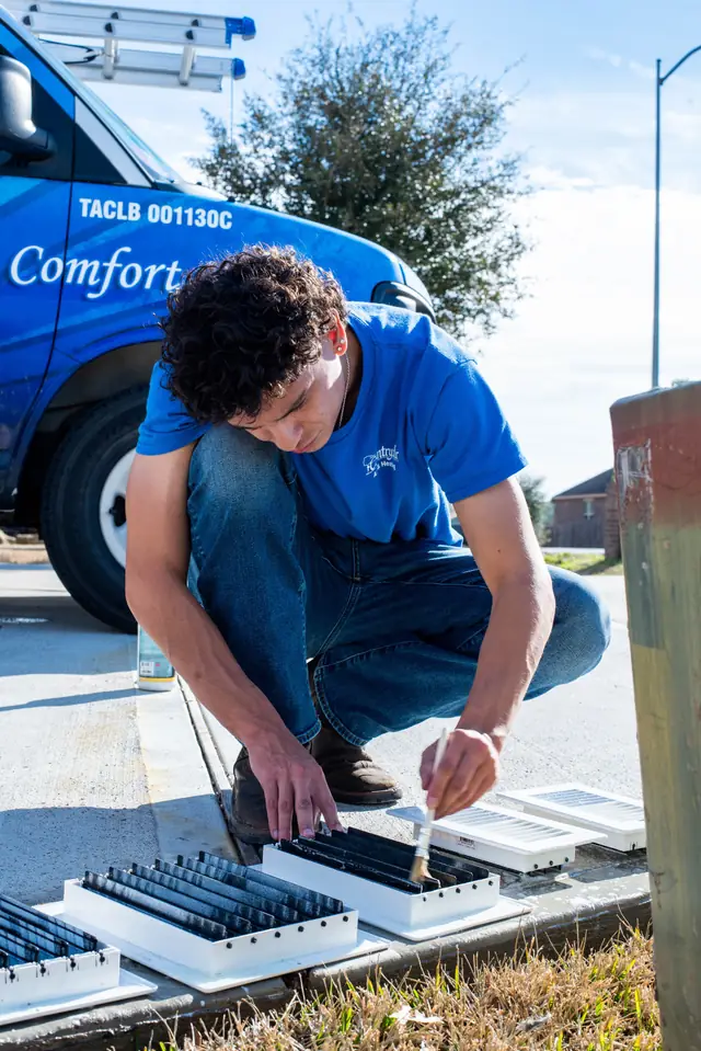 A Country Air technician servicing vent registers on a Magnolia driveway beside the branded company van